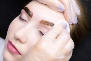 the master removes the remnants of paint from the eyebrows of the model with a cotton sponge photo