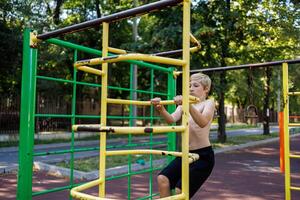 Deportes adolescente en el gimnástico escalera en el parque. calle rutina de ejercicio en un horizontal bar en el colegio parque. foto