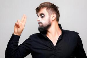 a man with undead makeup for Halloween holds his hands in front of him and looks at the camera from under his forehead photo