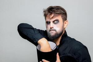 a man with a beard and makeup for Halloween holds a black box with gifts in his hands photo