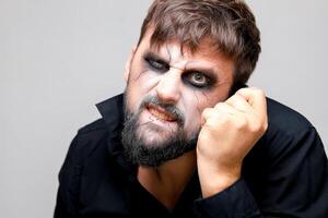 retrato de un barbado hombre con estilo no-muerto maquillaje quien sostiene su mano cerca su cabeza foto