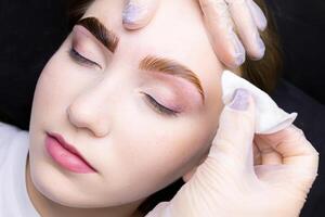 the master removes the remnants of paint from the eyebrows of the model with a cotton sponge photo