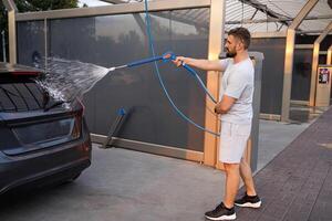A man points a foam sprayer at a car. A car at a self service car wash. photo