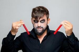 a bearded man with undead makeup for Halloween holds test tubes in which red liquid photo