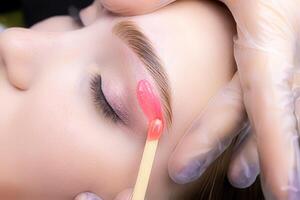 close-up of applying red wax to remove unwanted hairs from the lower contour of the model's eyebrows photo
