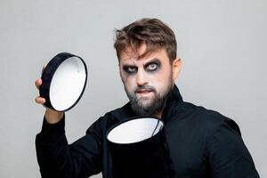A bearded man with undead-style makeup opens a black box for Halloween photo