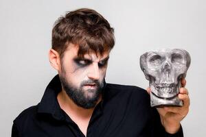 un hombre en el estilo de muertos vivientes maquillaje sostiene un casco en su mano foto