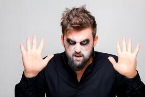 a man with undead makeup for Halloween holds his hands in front of him and looks at the camera from under his forehead photo