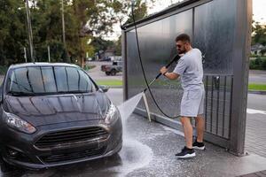 The front part of the car being washed by a man using a water cannon. A car at a self service car wash. photo