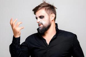 Scary undead-style makeup for Halloween on a bearded man who shows gestures photo