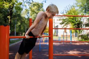 Athletic boy stretched upward and holding onto the tourniquet with his hands. Street workout on a horizontal bar in the school park. photo