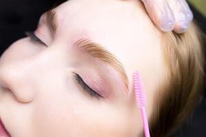 a close-up of the eyebrows on which lamination is performed and the master combs with a brush directing the growth of eyebrow hair photo