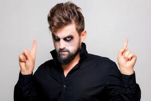 a man with undead makeup for Halloween holds his hands in front of him and looks at the camera from under his forehead photo