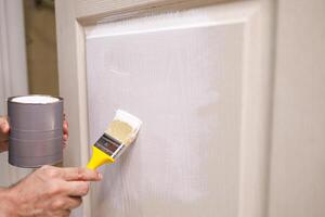 In his hands is a can of paint and a brush with which to apply the paint to the wooden door. Repair staining the doors with paint. photo