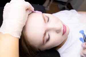 the model's face in close-up combs the model's eyebrows with a pink brush after lamination photo