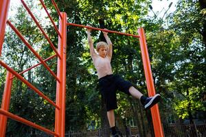 Athletic teenager grabbed the crossbar and swings. Street workout on a horizontal bar in the school park. photo