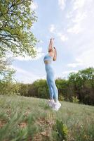 The girl in the park has her arms up and is doing pull-ups before her workout. Beautiful blonde Caucasian woman in blue tight tracksuit. Blonde girl at an outdoor training session photo