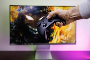 A man's hand holding a gamepad in front of the monitor. game gamepad in hand photo