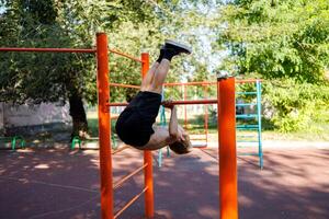 Athletic boy performs exercises on the bar. Street workout on a horizontal bar in the school park. photo