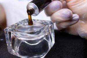 close-up of squeezing eyebrow paint from a tube into a glass cup photo