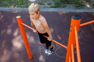 el adolescente estirado fuera en su manos y realiza acrobático ejercicios en el horizontal bar. calle rutina de ejercicio en un horizontal bar en el colegio parque. foto