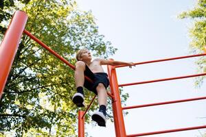 A teenager who has climbed a gymnastics bar sits and rests. Street workout on a horizontal bar in the school park. photo