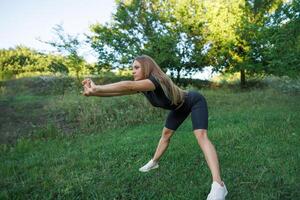 A young girl does a warm-up before a workout. Athletic girl in a tight uniform working outdoors in the park. photo