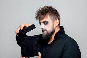 A bearded man with undead-style makeup opens a black box for Halloween photo