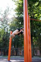 A teenager in a park playing sports hangs upside down on a crossbar. Street workout on a horizontal bar in the school park. photo