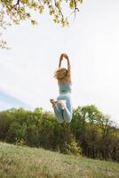 Bottom view of a girl athlete jumping in the background of the park. Beautiful blonde Caucasian woman in blue tight tracksuit. Blonde girl at an outdoor training session photo
