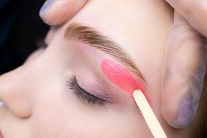 close-up of applying red wax to remove unwanted hairs from the lower contour of the model's eyebrows photo