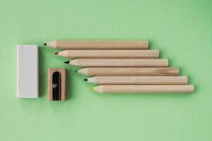 Colored pencils, wooden manual sharpener and eraser on green background. Back to school concept. Set of writing tools for education, creativity, drawing, hobby, art. Eco-friendly stationery photo