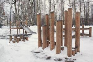 Wooden playground made of natural eco-friendly material in public city park with snow at winter time. Modern safety children outdoor equipment. Winter activities. Children rest and games on open air photo