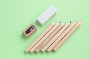 Colored pencils, wooden manual sharpener and eraser on green background. Back to school concept. Set of writing tools for education, creativity, drawing, hobby, art. Eco-friendly stationery photo