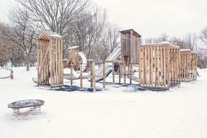 Wooden playground made of natural eco-friendly material in public city park with snow at winter time. Modern safety children outdoor equipment. Winter activities. Children rest and games on open air photo