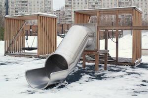 Wooden playground made of natural eco-friendly material in public city park with snow at winter time. Modern safety children outdoor equipment. Winter activities. Children rest and games on open air photo