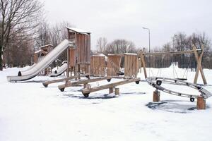 de madera patio de recreo hecho de natural Respetuoso del medio ambiente material en público ciudad parque con nieve a invierno tiempo. moderno la seguridad niños al aire libre equipo. invierno actividades. niños descanso y juegos en abierto aire foto