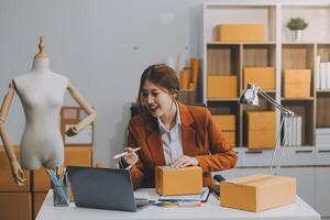 Emprendedor autónomo de pequeñas empresas, retrato de mujer joven que trabaja en la oficina del hogar, caja, teléfono inteligente, computadora portátil, en línea, marketing, empaque, entrega, pyme, concepto de comercio electrónico foto