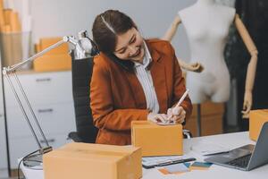 Emprendedor autónomo de pequeñas empresas, retrato de mujer joven que trabaja en la oficina del hogar, caja, teléfono inteligente, computadora portátil, en línea, marketing, empaque, entrega, pyme, concepto de comercio electrónico foto