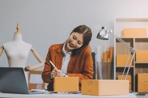 Emprendedor autónomo de pequeñas empresas, retrato de mujer joven que trabaja en la oficina del hogar, caja, teléfono inteligente, computadora portátil, en línea, marketing, empaque, entrega, pyme, concepto de comercio electrónico foto