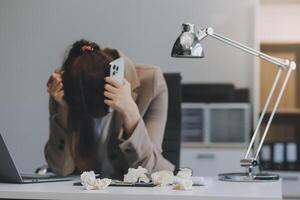 asiático mujer sentado en un oficina con estrés y ojo presion cansado, retrato de triste infeliz cansado frustrado decepcionado dama sufrimiento desde migraña sentado a el mesa, enfermo trabajador concepto foto