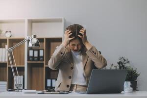 asiático mujer sentado en un oficina con estrés y ojo presion cansado, retrato de triste infeliz cansado frustrado decepcionado dama sufrimiento desde migraña sentado a el mesa, enfermo trabajador concepto foto