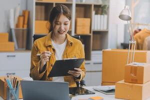 Las pymes asiáticas usan computadoras portátiles para verificar las cajas de envío en línea de pedidos de clientes en casa. Emprendedor de pequeñas empresas pyme freelance. negocio en línea, concepto de trabajo en casa. foto