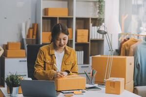 Las pymes asiáticas usan computadoras portátiles para verificar las cajas de envío en línea de pedidos de clientes en casa. Emprendedor de pequeñas empresas pyme freelance. negocio en línea, concepto de trabajo en casa. foto