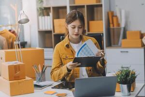 Las pymes asiáticas usan computadoras portátiles para verificar las cajas de envío en línea de pedidos de clientes en casa. Emprendedor de pequeñas empresas pyme freelance. negocio en línea, concepto de trabajo en casa. foto