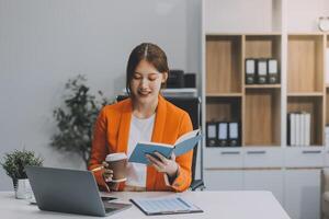 Beautiful smiling Asian businesswoman holding a coffee cup while taking notes at office. photo