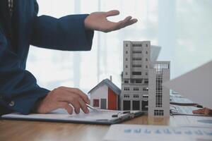 balancing the property sector The real estate agent is explaining the house style to see the house design and the purchase agreement.Wooden house at modern office photo