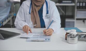 hembra médico sentado a escritorio y escritura un prescripción para su paciente foto