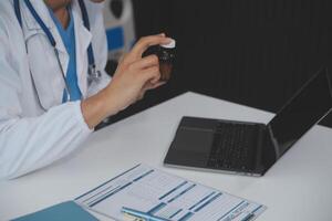 un profesional y enfocado asiático hembra médico en matorrales es trabajando y leyendo médico investigación en su ordenador portátil en su oficina a un hospital. foto