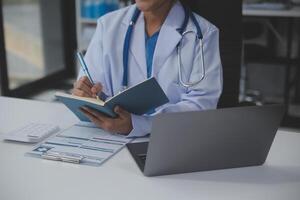 A professional and focused Asian female doctor in scrubs is working and reading medical research on her laptop in her office at a hospital. photo